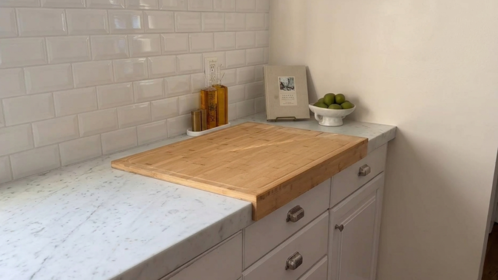 Large bamboo cutting board positioned over a kitchen countertop beside decorative kitchen accessories